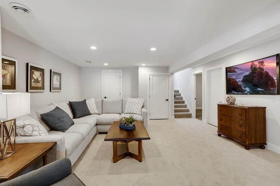 Bright finished basement with a grey sectional, wood coffee table, framed art and a staircase